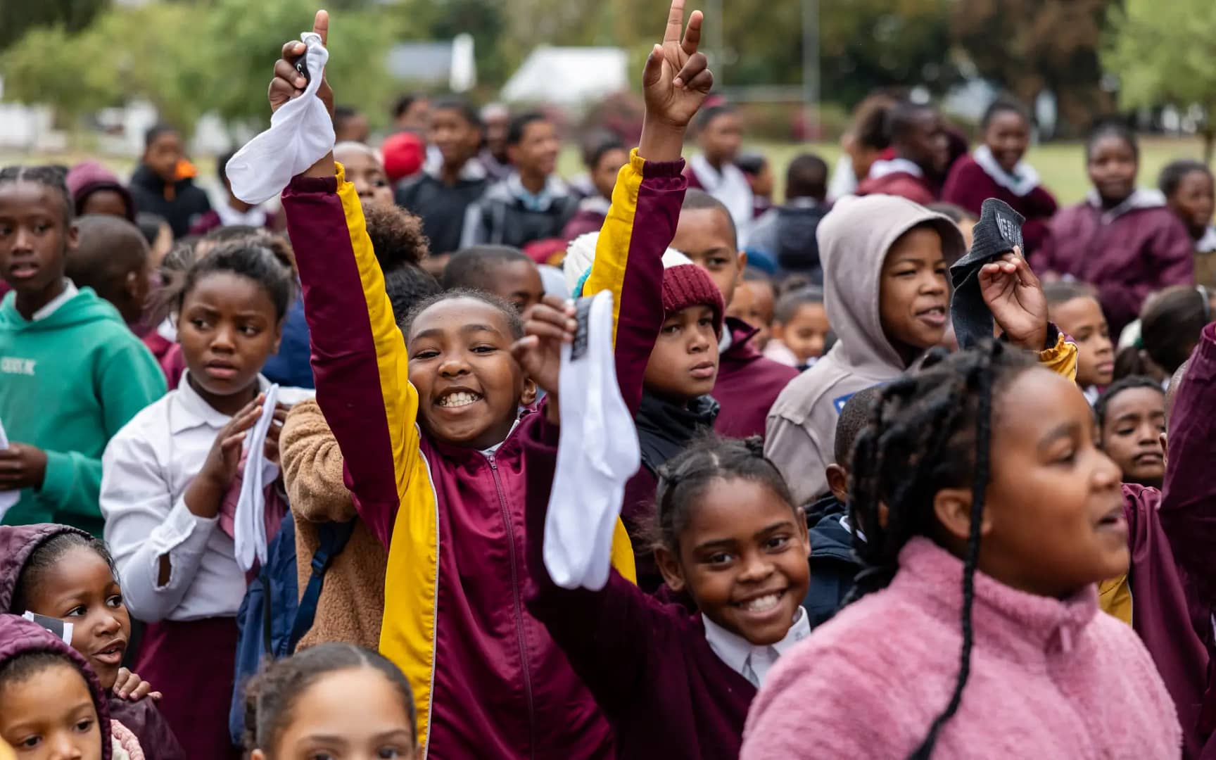 School children in maroon and yellow uniforms outdoors, waving black and white sexy socks